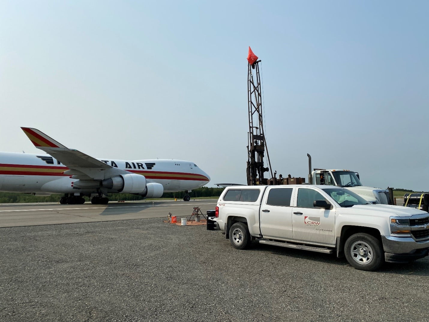 Photo of plane on runway, CRW truck, and drilling equipment